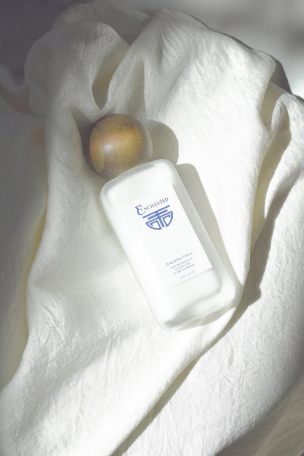 Enchanted Alchemy body and hair mist bottle with amber wooden cap  on white textured fabric